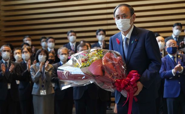 写真・図版 : 首相を辞任にあたり、花束を受け取り、一礼する菅義偉首相＝2021年10月4日、首相官邸