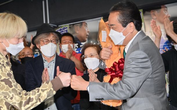 写真・図版 : 小選挙区で当選した菅直人氏（右）。支持者から花束を受け取った後、グータッチをした。前列左から2人目の帽子をかぶっている男性が筆者＝2021年11月1日、東京都武蔵野市