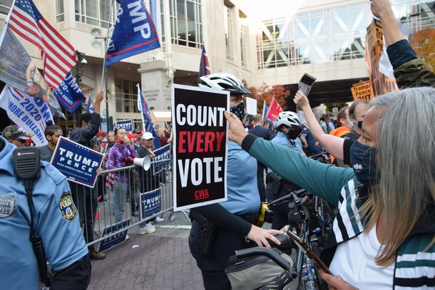 写真・図版 : 米大統領選の開票作業が続くペンシルベニア州フィラデルフィアで、警官隊を挟んでトランプ大統領の支持者とにらみ合い、気勢を上げるバイデン氏の支持者ら（右）＝2020年11月6日