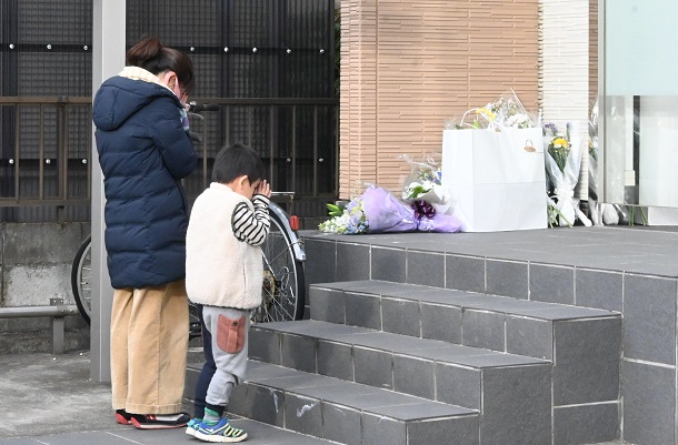 
亡くなった医師鈴木純一さんの在宅療養支援診療所の前で手を合わせる親子=2022年1月30日午後3時15分、埼玉県富士見市