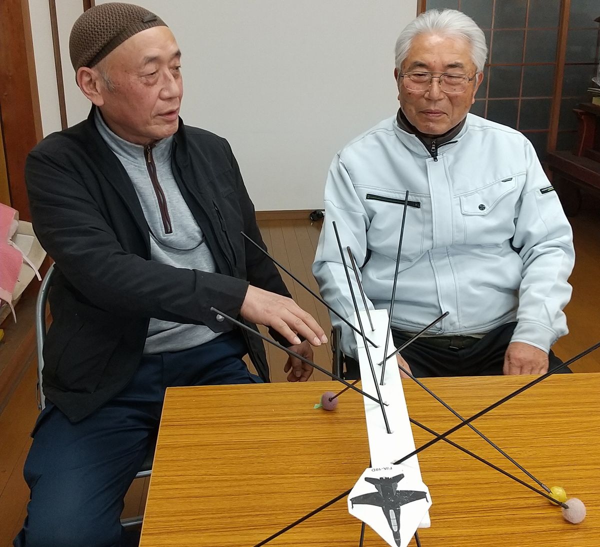 写真・図版 : 「写真や目撃証言があれば飛行高度は割り出せる」という大野智久さん（左）と秋山欣也さん。手前は複数の目撃証言を集めて飛行高度を推定する手法を説明するための模型＝2021年2月、岡山県倉敷市、筆者撮影