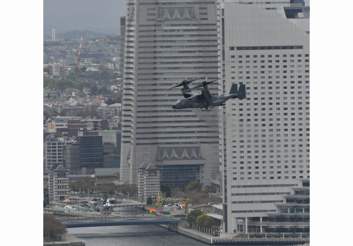 写真・図版 : 横浜の市街地上空を飛ぶ米軍の輸送機オスプレイ。後方はみなとみらい地区＝2018年4月5日