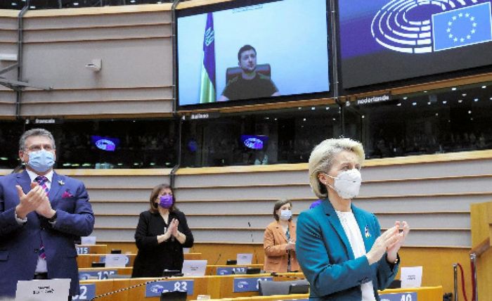 写真・図版 : ブリュッセルの欧州議会で、ウクライナのゼレンスキー大統領のビデオ演説に拍手を送るフォンデアライエン欧州委員長（手前右）＝2022年3月1日