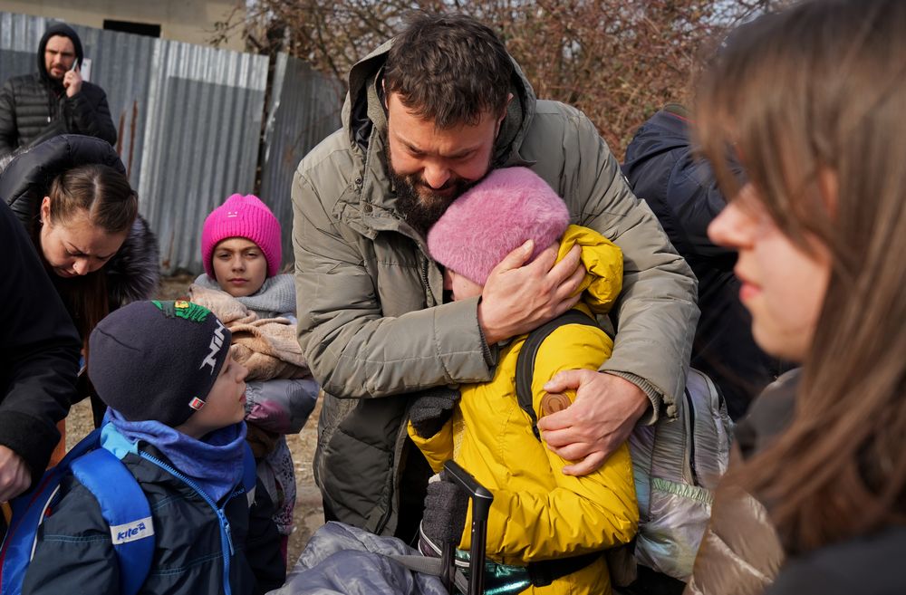 写真・図版 : 国境で引き裂かれる家族。総動員令によりウクライナを離れられない男性は、国外に逃れる家族と、別れを前に抱き合った＝2022年3月3日、ウクライナ西部ウジホロド