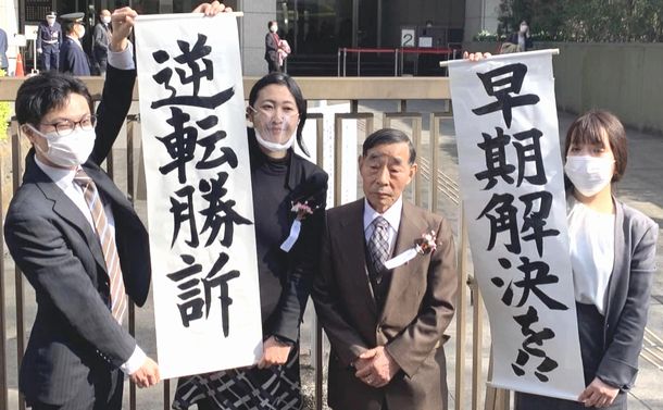 写真・図版 : 「逆転勝訴」を伝え、「早期解決を!!」と訴える北三郎さん（活動名、左から3人目）と弁護団。左から2番目が筆者＝2022年3月11日、東京高裁前、筆者提供