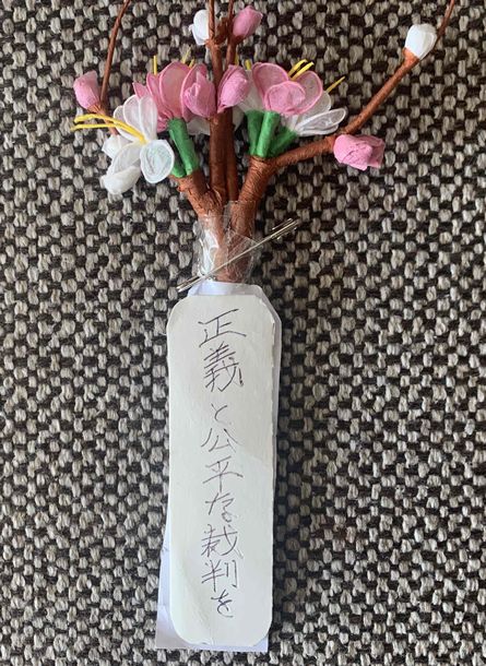 写真・図版 : 北三郎さんの胸の花は北さん作成。直筆で「正義と公平な裁判を」と書かれている＝筆者提供