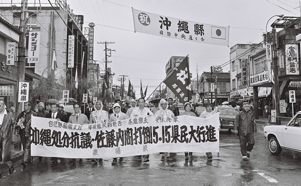 1972年5月15日 那覇市の国際通りで、沖縄の復帰を祝う横断幕の下を、復帰に反対してデモ行進する人たち