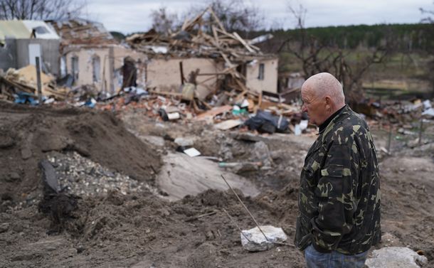 写真・図版 : ロシア軍の攻撃によって破壊された住宅の前を歩く男性＝2022年4月19日、ウクライナ・イワンキフ