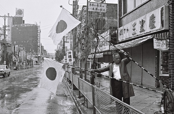 写真・図版 : 復帰の日の朝、那覇市の国際通りに日の丸を揚げる市民=1972年5月15日