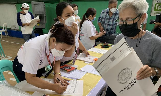 写真・図版 : フィリピン大統領選でマークシート式の投票用紙を受け取る有権者（右）＝2022年5月9日、マニラ首都圏ケソン