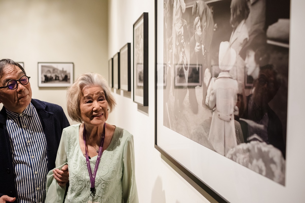 写真・図版 : 『BeHere / 1942』展で、自身の強制収容の体験が写っている写真を見るタニオカ・ミチさんとメディア・アーティストの藤幡正樹さん＝ロサンゼルスの全米日系人博物館、Ning Wong Studios