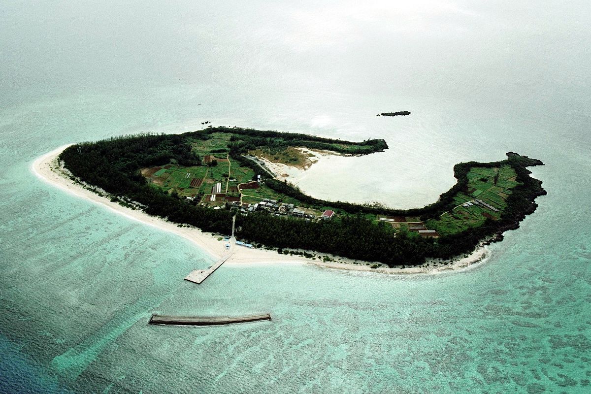 写真・図版 : 沖縄本島北部の本部半島沖にある水納島。クロワッサンのような形をしている＝1991年、朝日新聞社機から