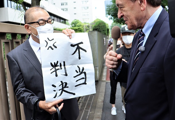 写真・図版 : 東京高裁判決を受けて「不当判決」と欠かれた紙を掲げるDHCテレビジョンの山田晃社長（左）とケント・ギルバート氏＝2022年6月3日、東京高裁前、筆者撮影