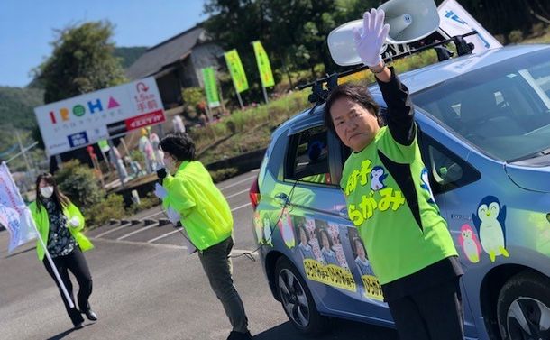 写真・図版 : 選挙カーの前で手を振る平神純子さん