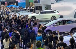 写真・図版 : 電池はEVの中核技術でもある。中国の新興EVメーカーが発表した新型車（中央の白い車）には、多くのメディア関係者らが詰めかけた＝2021年11月、広州