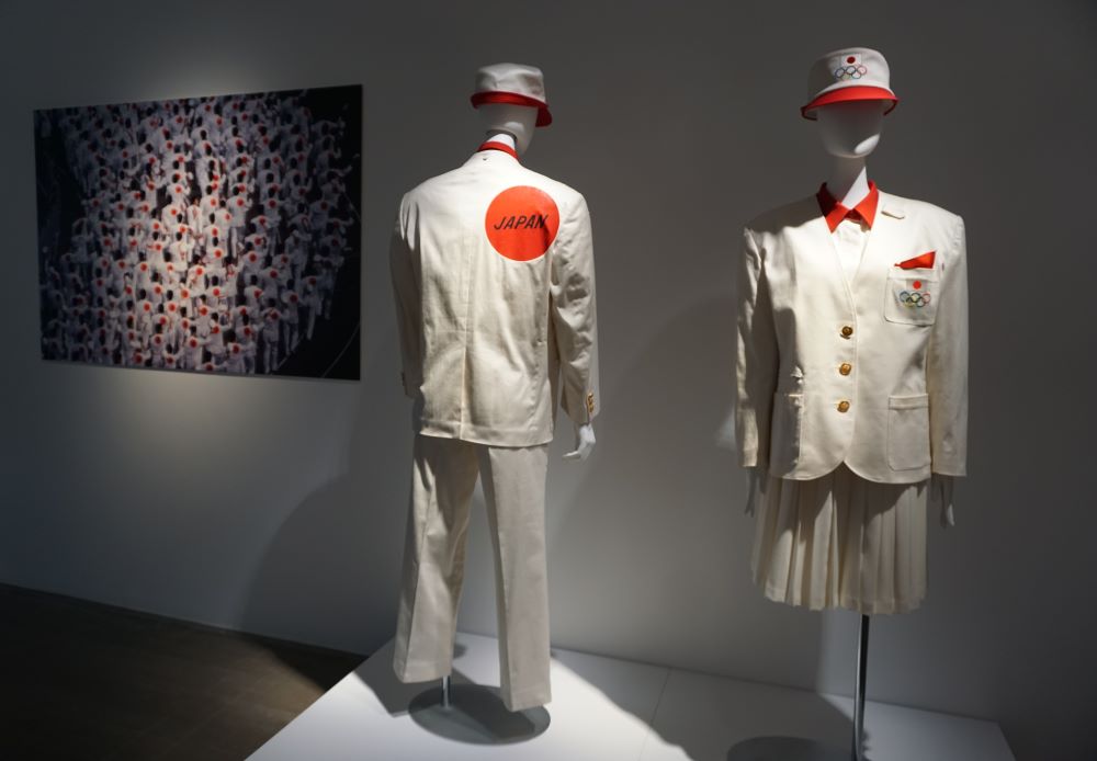 写真・図版 : 森英恵さんがデザインした1992年バルセロナ五輪の日本選手団公式服。左に行進風景の写真が見える＝2020年2月、水戸芸術館現代美術ギャラリー