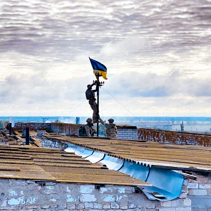 写真・図版 : ロシア軍の支配下にあった南部ヘルソン州の集落にある建物の屋上で、ウクライナの国旗を立てるウクライナ軍兵士とされる写真。ウクライナのティモシェンコ大統領府副長官がフェイスブックに投稿した　2022年9月5日
