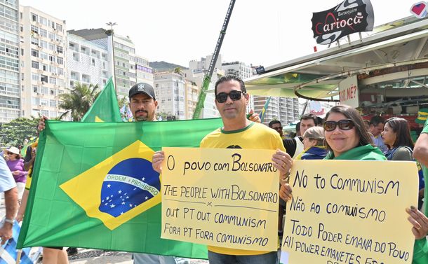 写真・図版 : 「人々はボルソナーロと共にある」と書いた紙を掲げるボルソナーロ大統領の支持者ら＝2022年9月7日、ブラジル・リオデジャネイロ