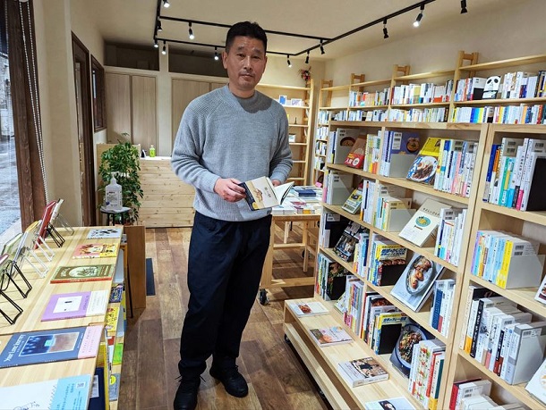 食関連の棚の前に立つ、ご店主の加茂和弘さん。天井がやや低く見えるのは、加茂さんが立派な体格をお持ちだから=撮影・筆者