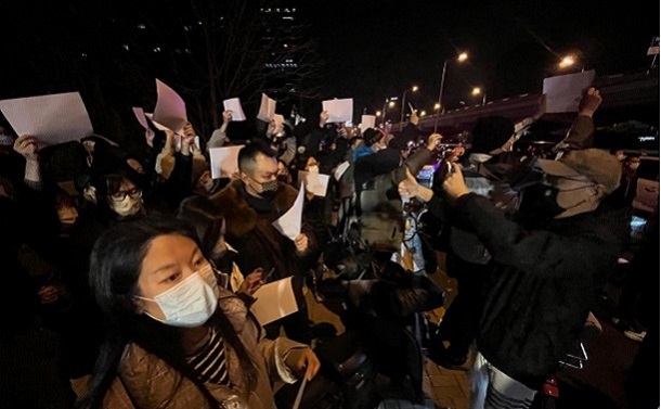 写真・図版 : 白い紙を掲げて「ゼロコロナ政策」への抗議の意思を示す人びと＝2022年11月27日 、北京市中心部