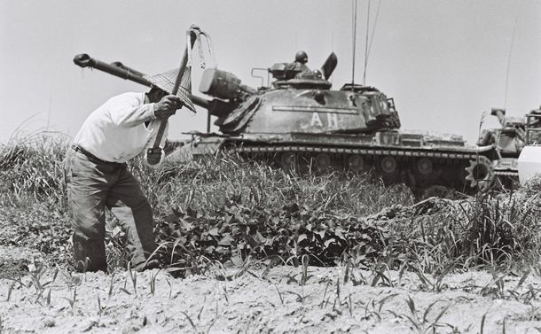 写真・図版 : 軍用地内での耕作が許された黙認耕作地で働く農夫の前を走る米軍の戦車。米軍が「銃剣とブルドーザー」で住民から強制収用した軍用地には、沖縄返還後も引き続き米軍に提供されたままの土地がある。住民の手には戻らなかった＝1971年5月7日、沖縄・読谷村
