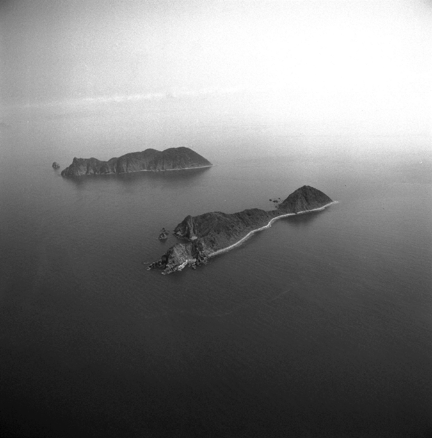 写真・図版 : １９８０年９月２日に撮影された福岡県北九州市若松区沖の響灘に浮かぶ白島。下が男島、上は女島。男島には石油備蓄基地がつくられた 