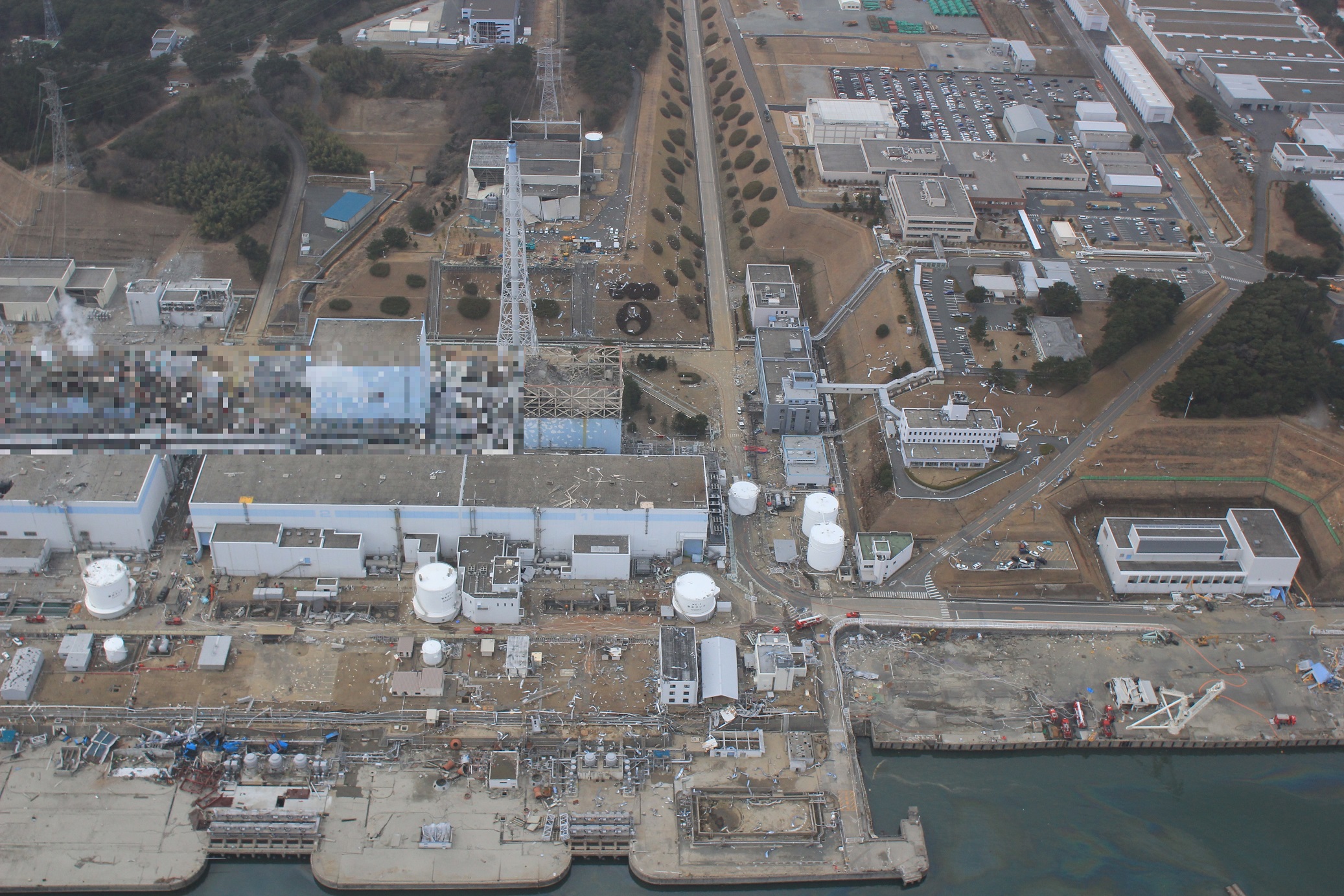 写真・図版 : 福島第一原発１、２号機（手前）と免震重要棟（右奥）＝東京電力ホールディングスが2020年12月22日に公表した2011年3月20日撮影の「福島第一原子力発電所事故の状況に係る写真」